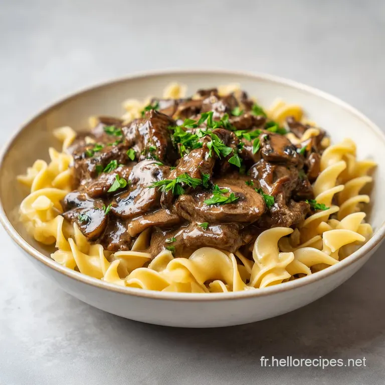 Elegant portion of stroganoff over buttered noodles, dollop of sour cream, vibrant green parsley, warm & inviting.